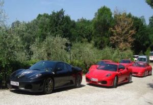 Lej en sportsvogn. Billede af italienske sportsvogne, der holder efter hinanden. Røde Ferrari og sort Porche. Bilerne holder på en grusvej i Italien.