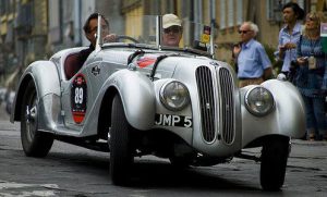 Billede af ældre italiensk sportsvogn i sølvfarve med to passagerer.